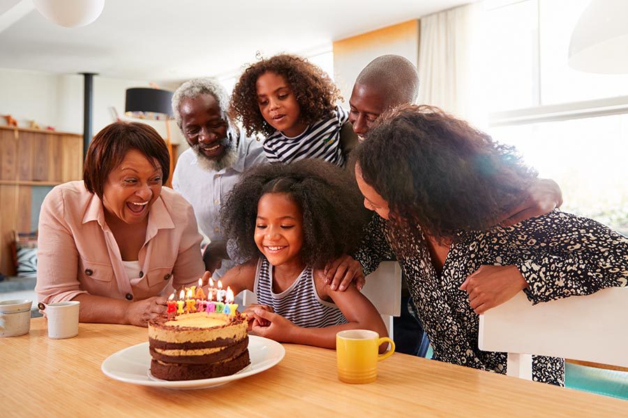 Personal Insurance - Extended Family Sings to a Young Girl Ready to Blow Out Her Birthday Candles on a Homemade Chocolate Cake at the Kitchen Table